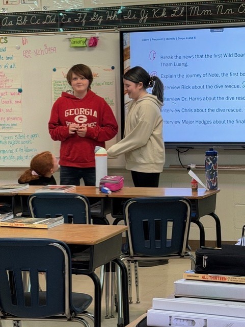 There is a boy and a girl in front of the room talking.