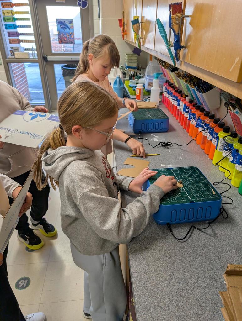 Two girls are standing at a counter cutting cardboard with the Chompsaws.