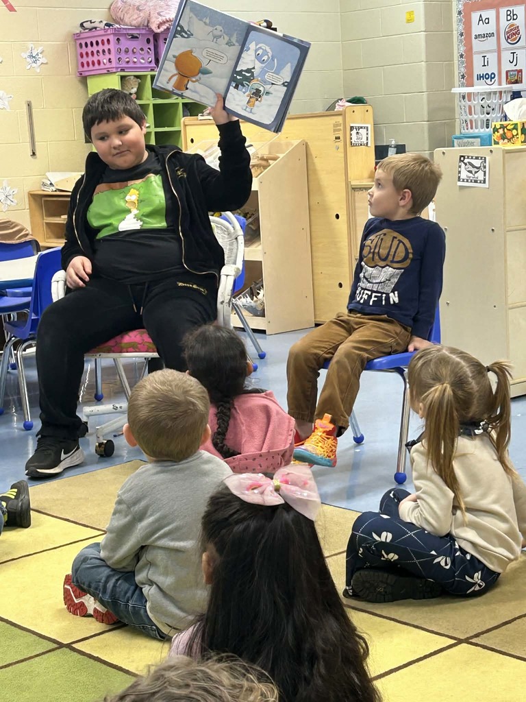 Older student reading book to younger students