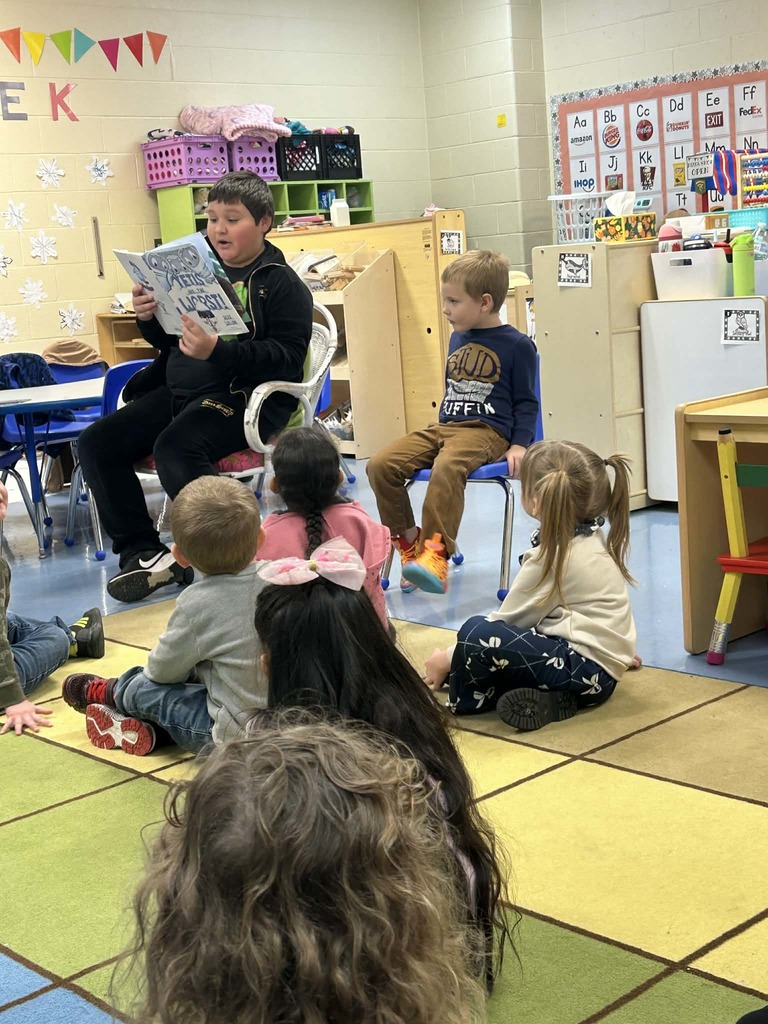 Older student reading book to younger students