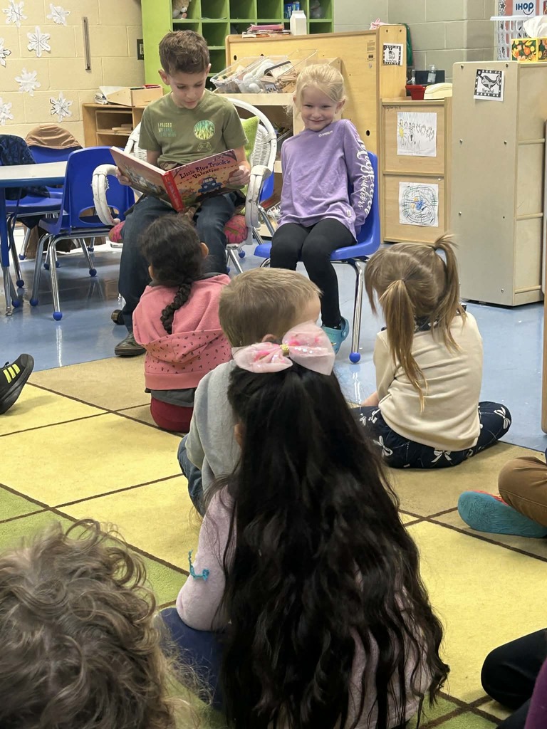 Older student reading book to younger students