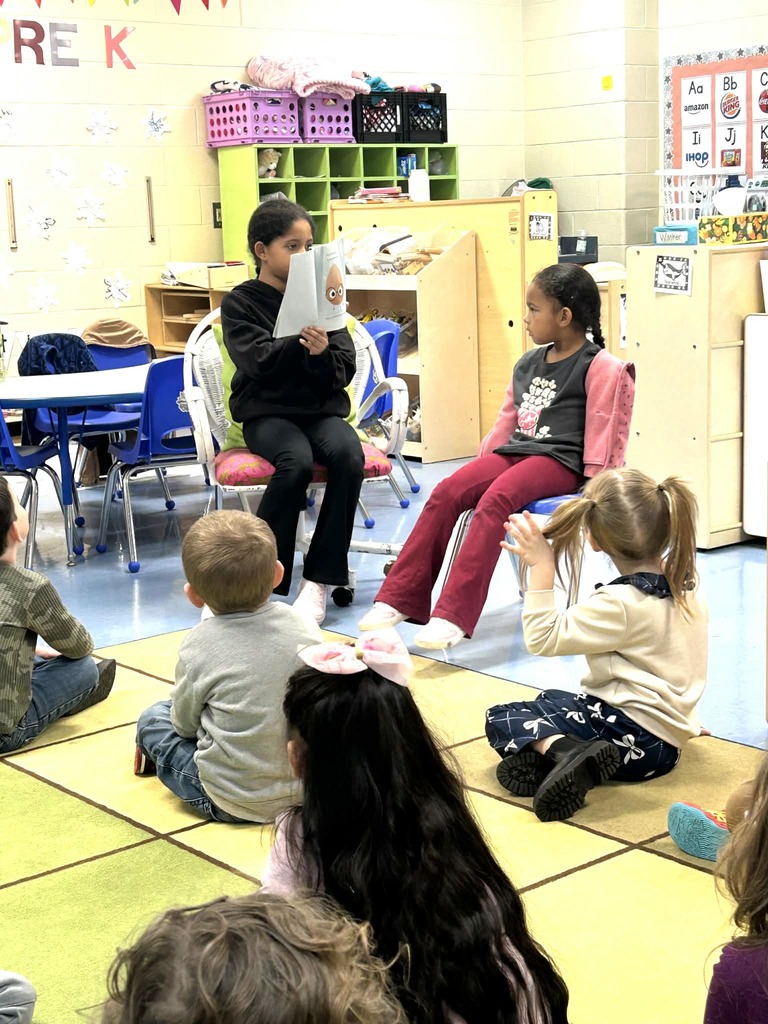 Older student reading book to younger students
