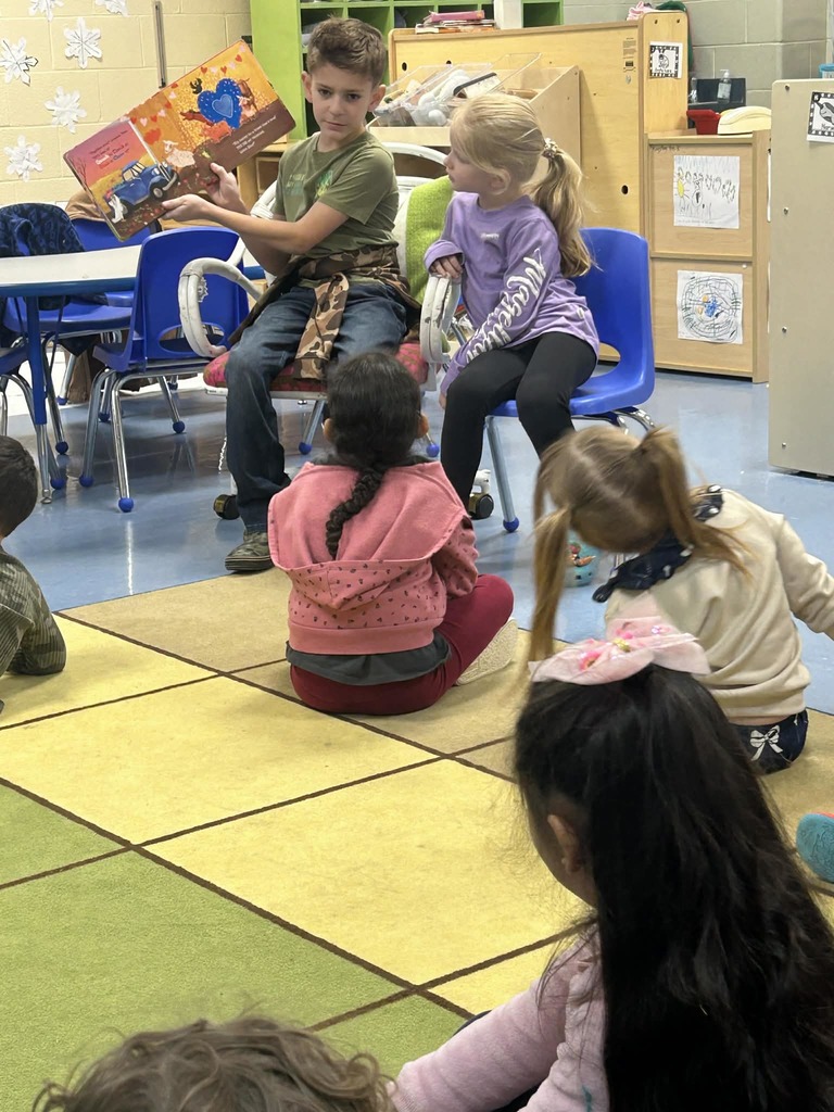 Older student reading book to younger students