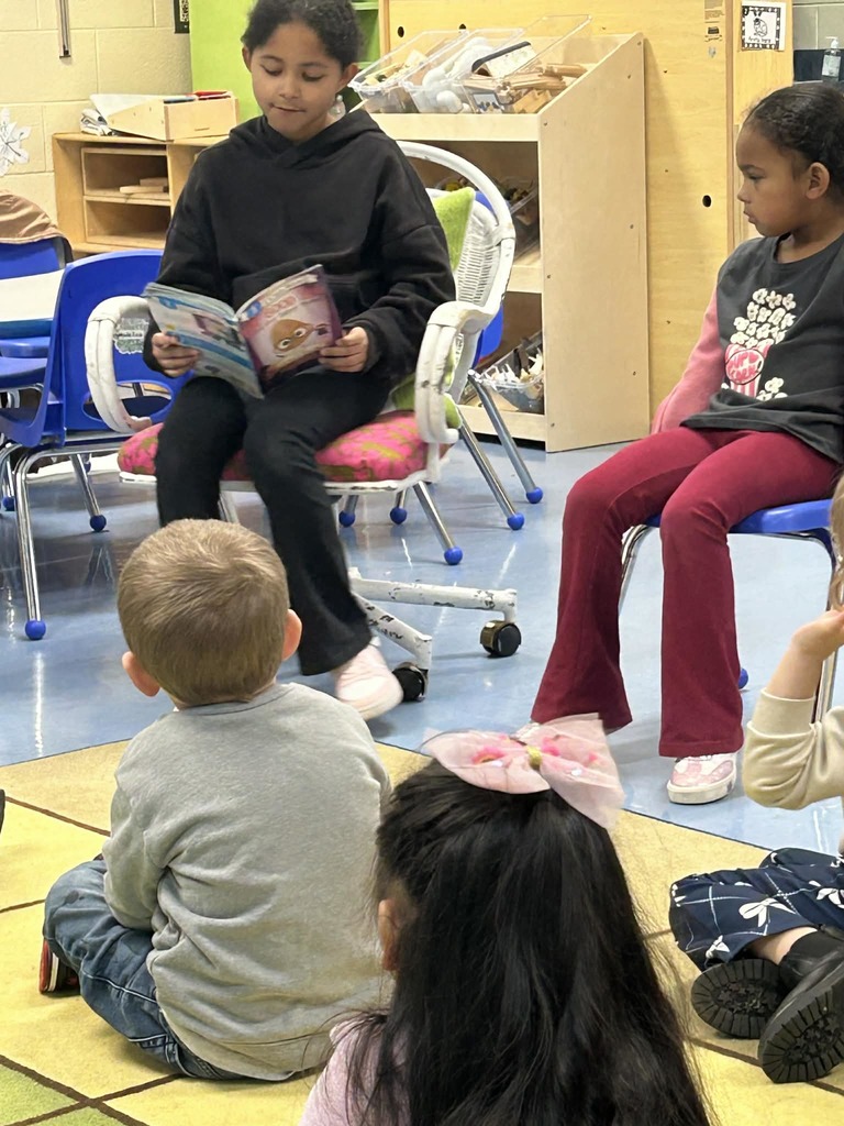 Older student reading book to younger students