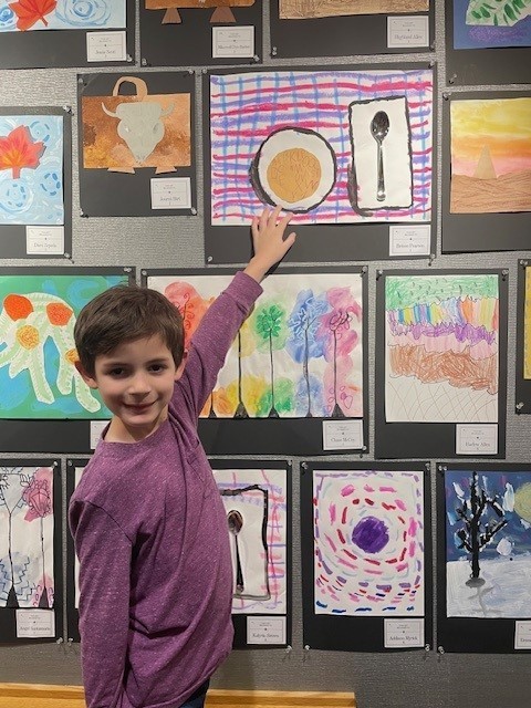 Student smiling for a picture showing his artwork. 