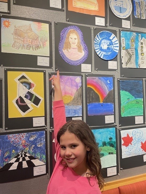 Student smiling and pointing at her artwork. 