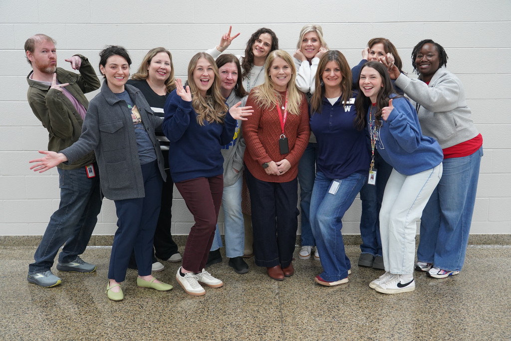 A group of adults smiling and posing with arms around each other in a room.