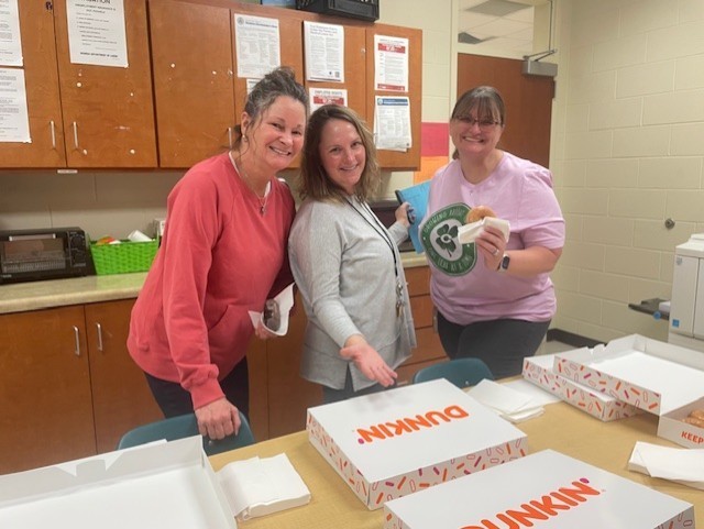 three staff members smiling for the camera and posing with Dunkin Donut boxes and donuts