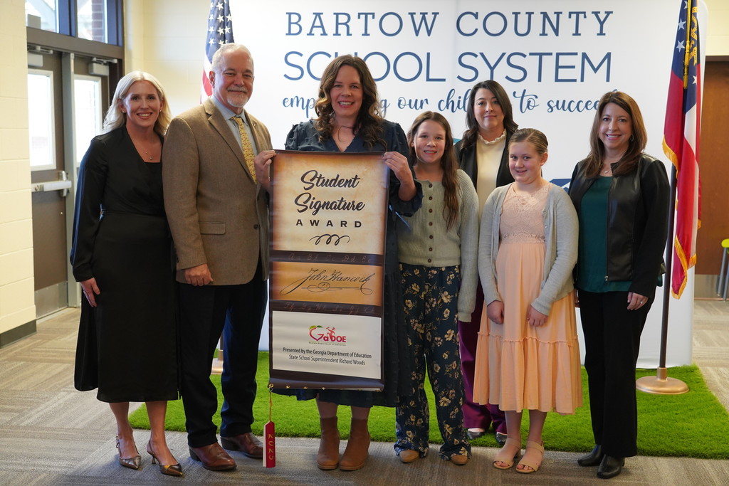 A group of adults and children stand together in front of a sign that reads "Bartow County School System".