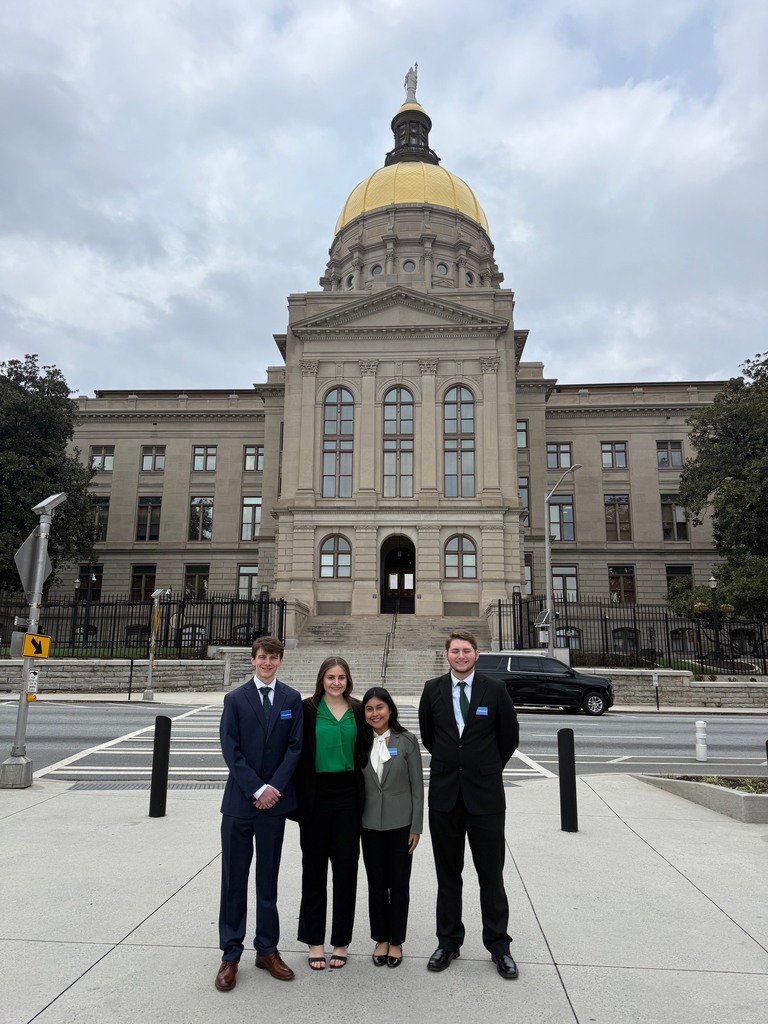Four people in suits stand in front of a government building with a dome.