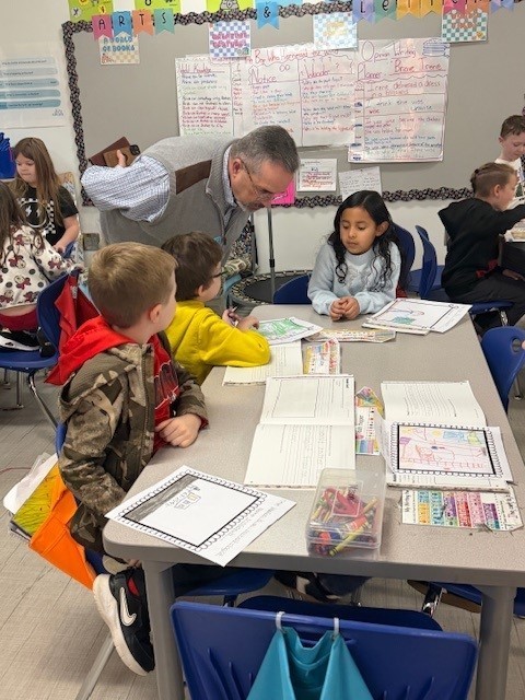 Mr. Emerson listening to a group of first grade students discuss their opinion writing. 
