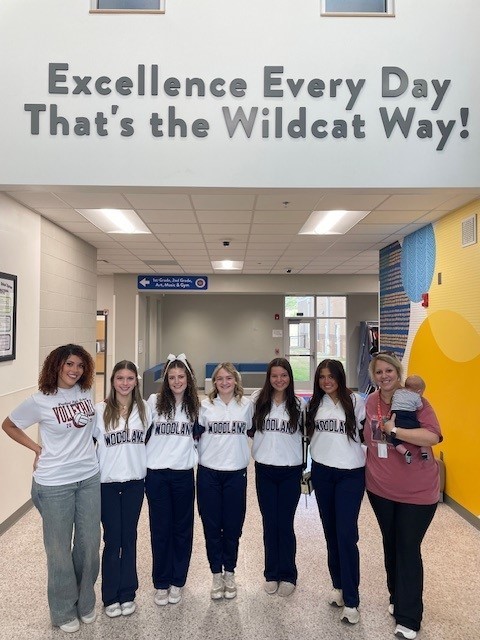 High School cheerleaders and coach smiling for a picture in the hallway.