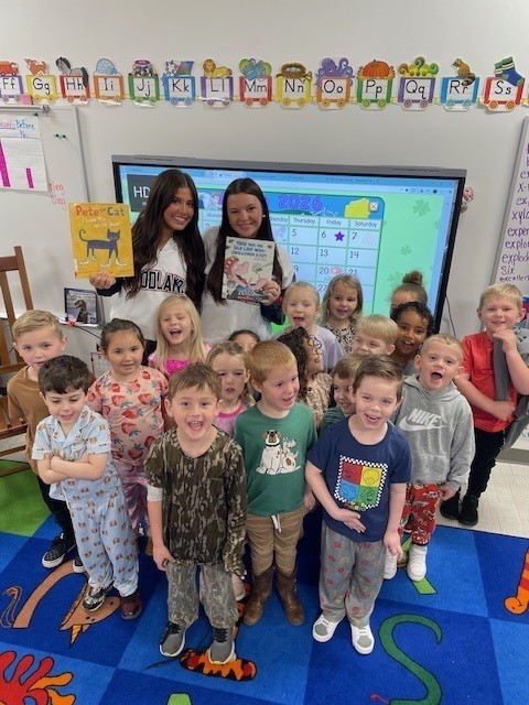 Highschool cheerleaders smiling for a picture with a PreK class after reading a book to them.