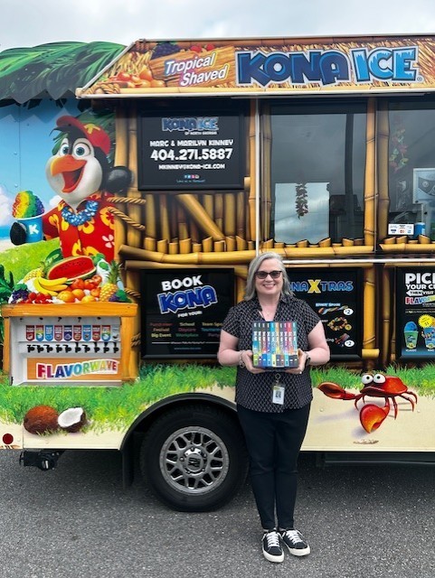 Woman with sunglasses stands next to a colorful ice cream truck with a cartoon character and tropical scenery.