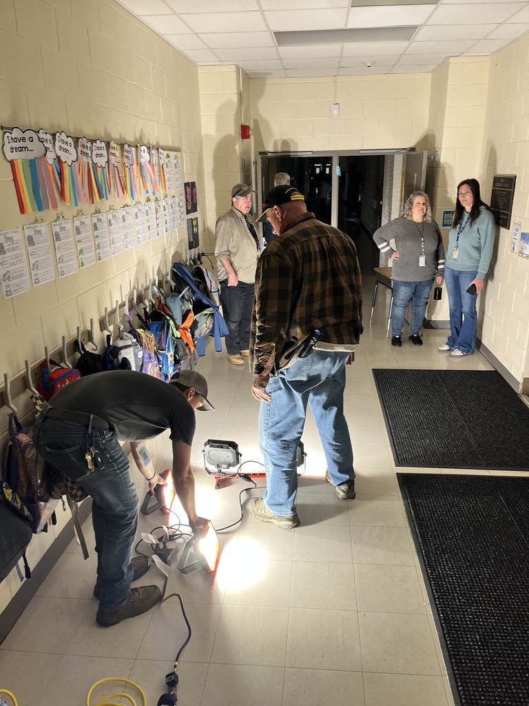 A hallway with white walls, black carpets, and various items on the wall. Several people are working on a task.
