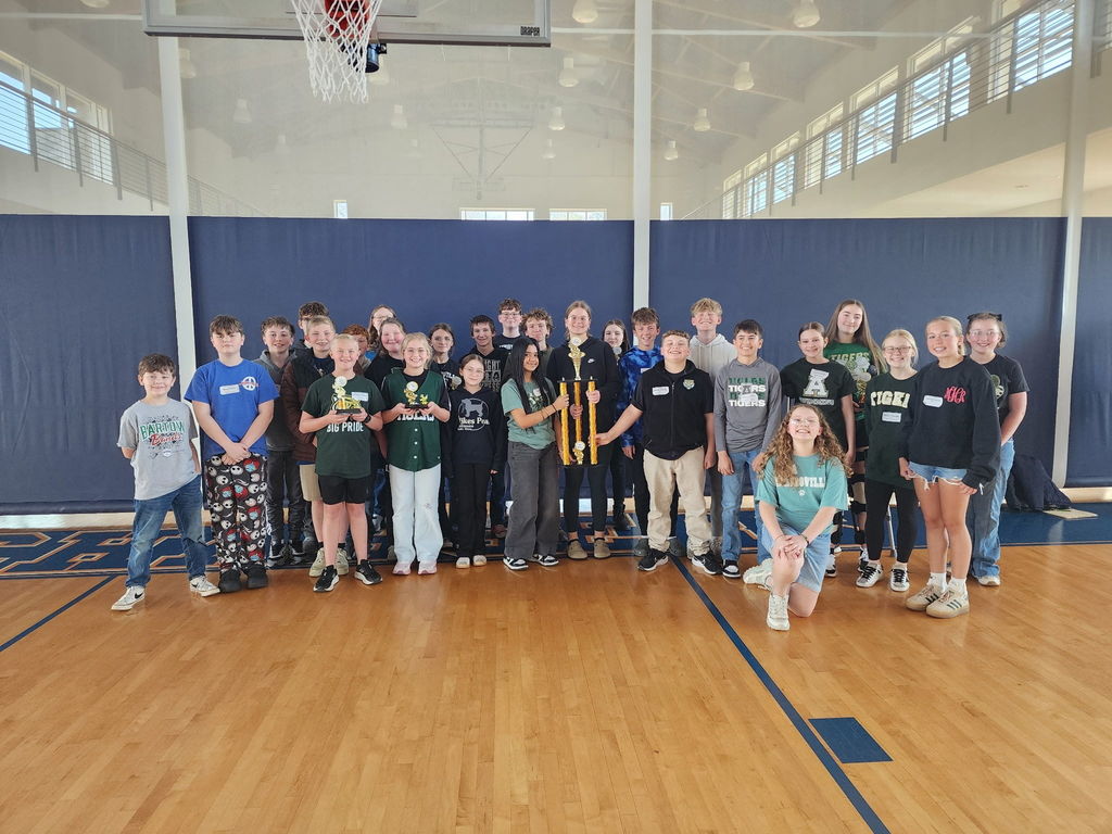 A group of students stands on a basketball court, holding trophies and posing for a photo.