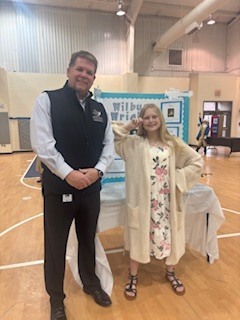 Man and girl posing with a display banner behind them in a gymnasium.