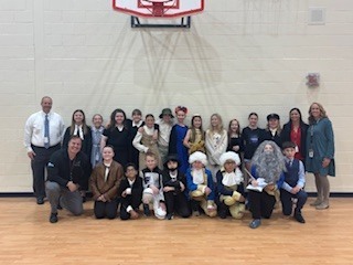 Group of students and adults in various costumes pose for a photo in a gymnasium.