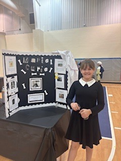 Person in a black dress standing in front of a display with pictures and text.