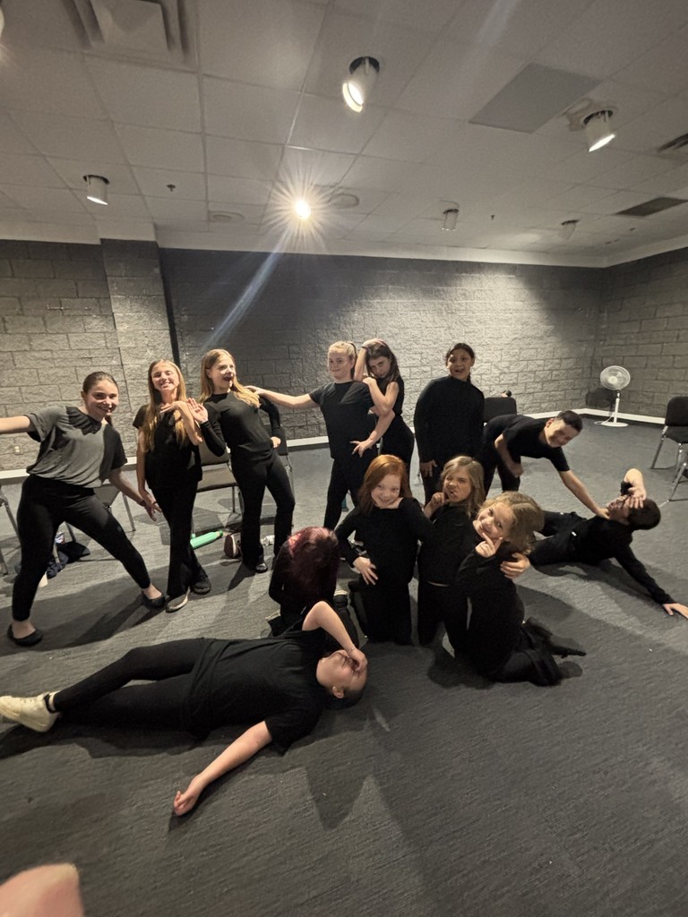 Group of adults and children in black clothes in a studio. Most are standing, some are lying down.