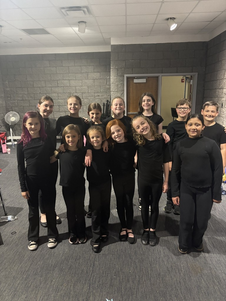 A group of children dressed in black attire pose for a photo in a room with gray walls and a ceiling.
