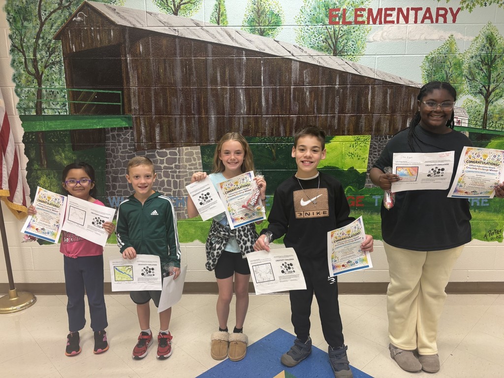 A group of five children stands in front of a backdrop of a bridge, holding papers.