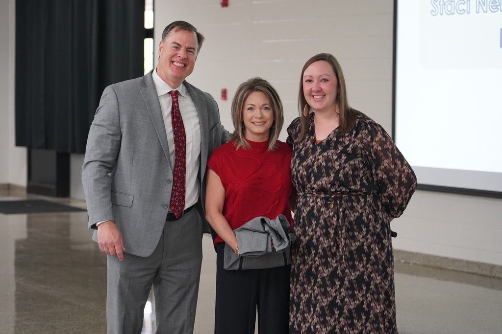 Three individuals pose for a picture in front of a large white projector screen in an indoor room.