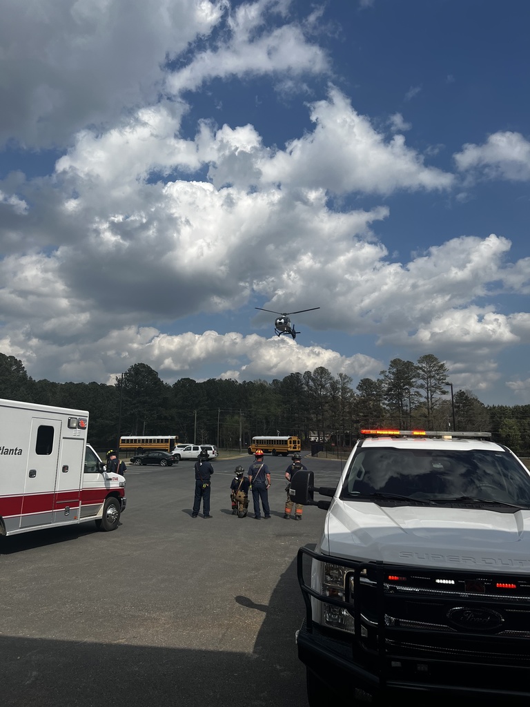 A helicopter in the sky above an emergency vehicle and people on the ground in a parking lot.