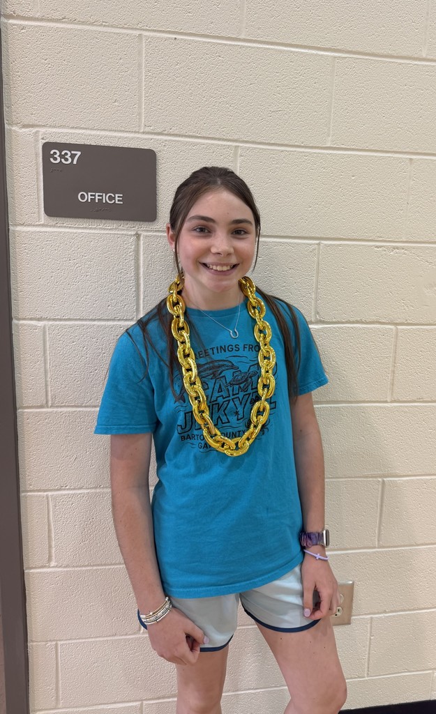 A young girl in a blue shirt and yellow necklace stands near a white brick wall. Above her, a gray sign reads "337 OFFICE."