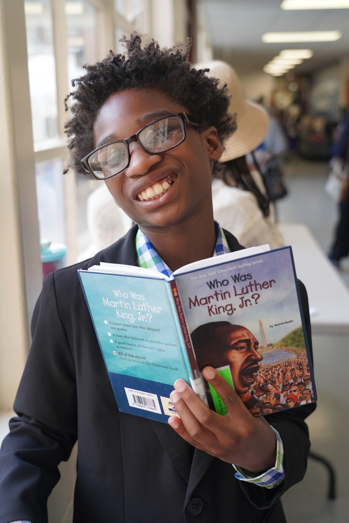 A person wearing glasses holds a book titled "Who Was Martin Luther King Jr?" They smile for the camera.