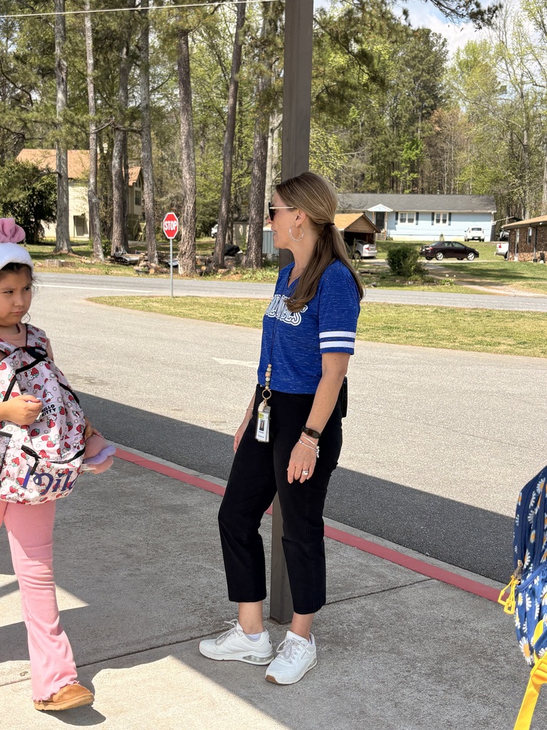 A woman in a blue shirt stands on a sidewalk near a young girl wearing a backpack.