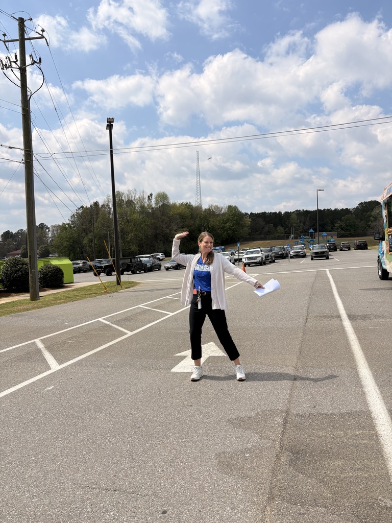 Person in a white sweater and black pants, holding a paper, stands in the middle of a road.