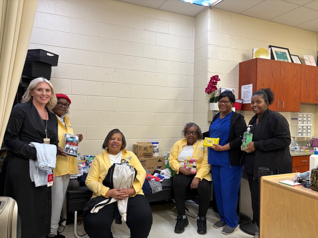 Five women in a room. Four of them hold gifts, and one woman has a white towel.