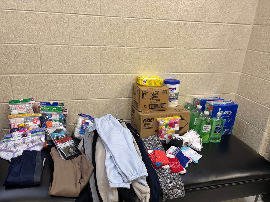 A table with clothes, hygiene products, and personal items on it against a white wall.