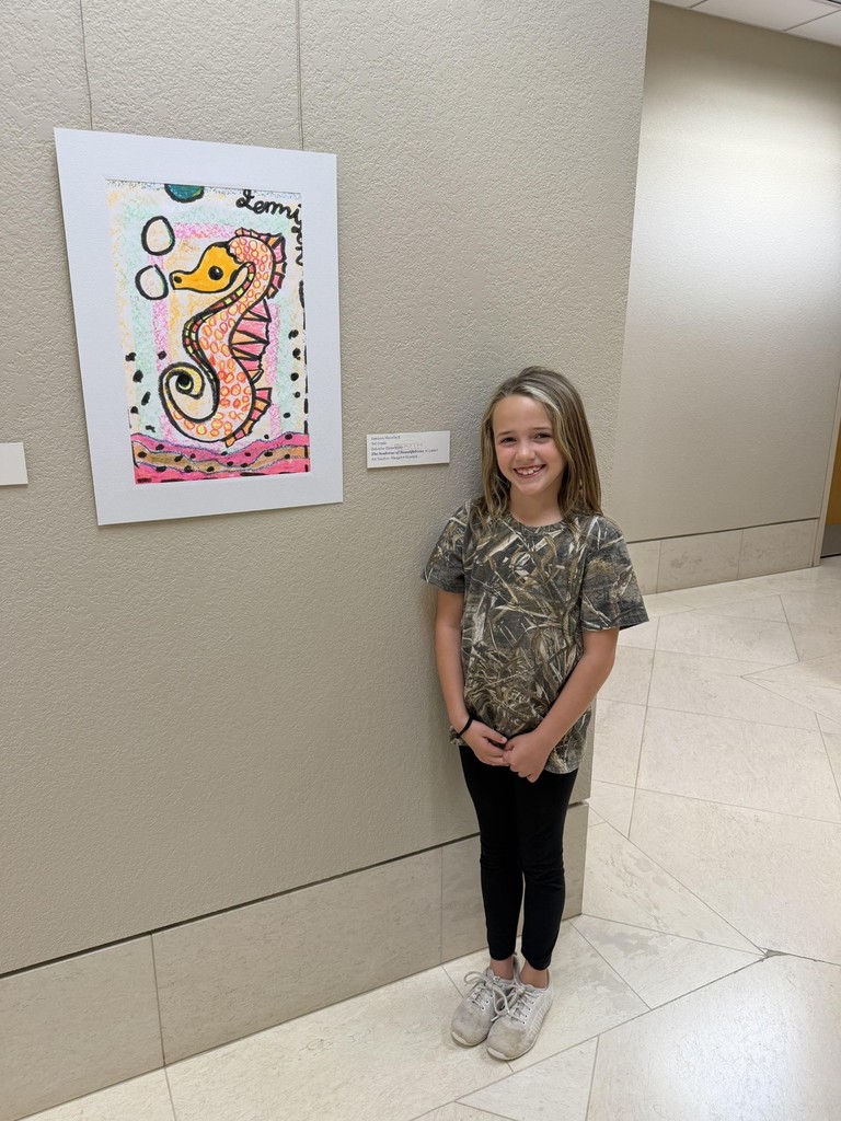 A girl stands in a hallway by a wall with a colorful painting of a seahorse.