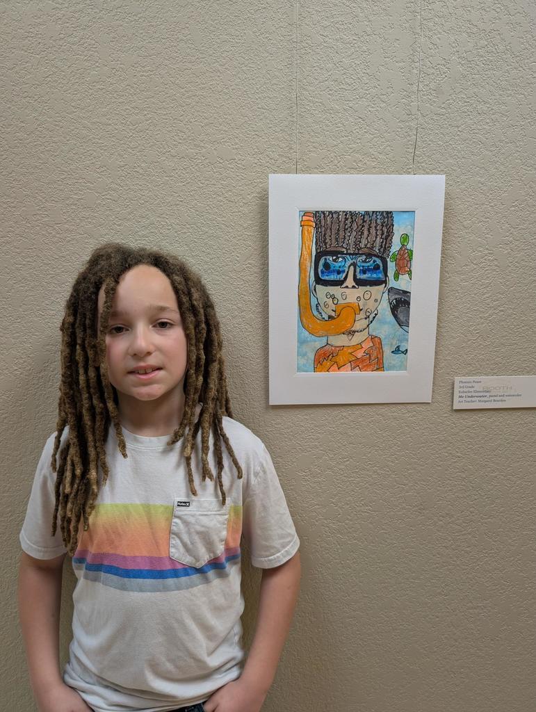 Child with dreadlocks and rainbow-colored t-shirt stands next to a framed artwork of a snorkeling person.