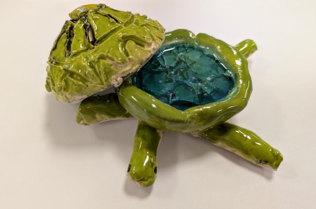Small green ceramic turtle with open shell revealing a blue interior. The turtle's shell and body have textured surfaces.