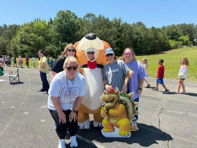 A group of five adults standing next to a large inflatable mascot in a parking lot.