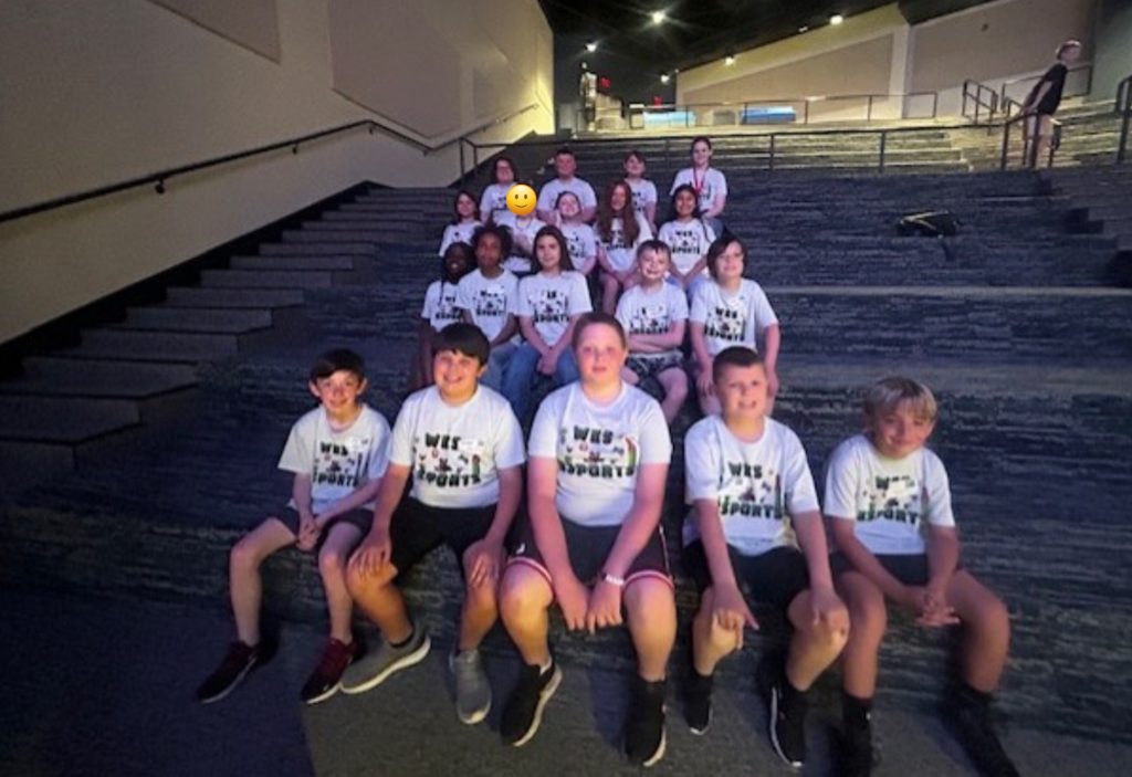 Group of people in matching shirts seated on steps of a stadium. Some people are standing behind them.