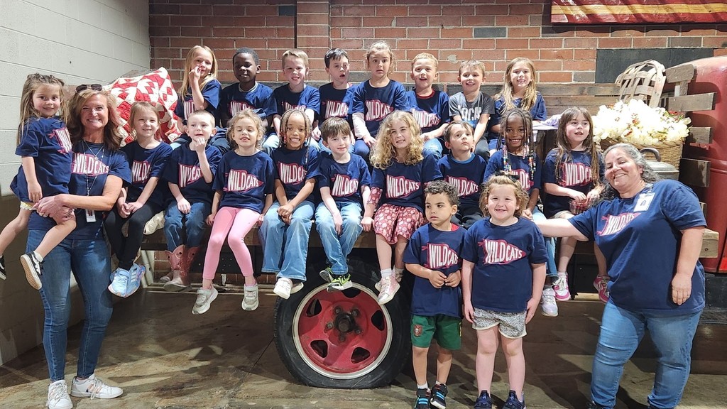 Children and adults in blue shirts pose in front of a red brick wall and a red wheel.