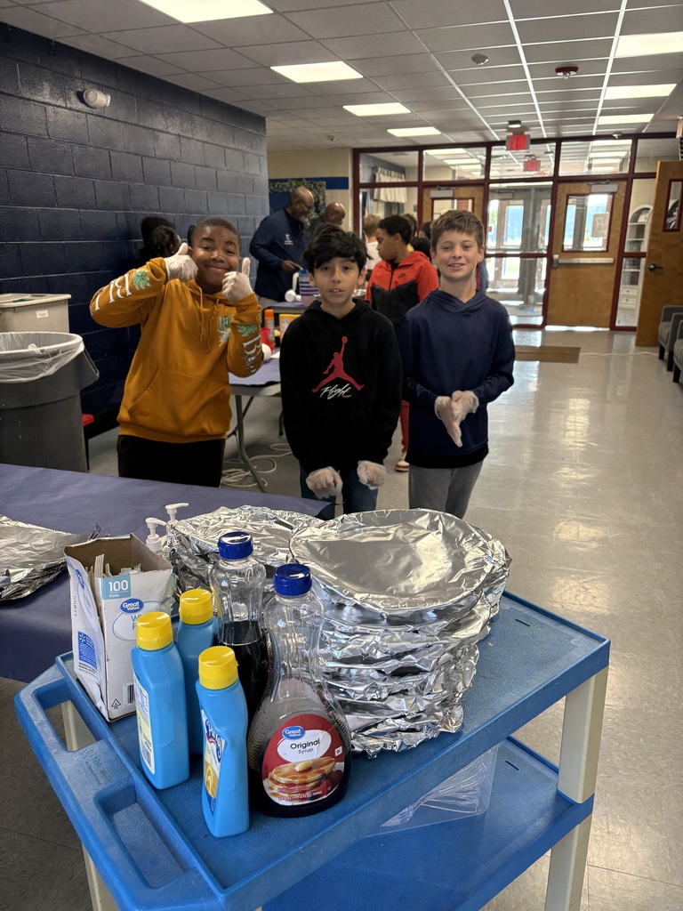 Three children in a room with a blue table, aluminum foil, bottles, and boxes, in a school setting.