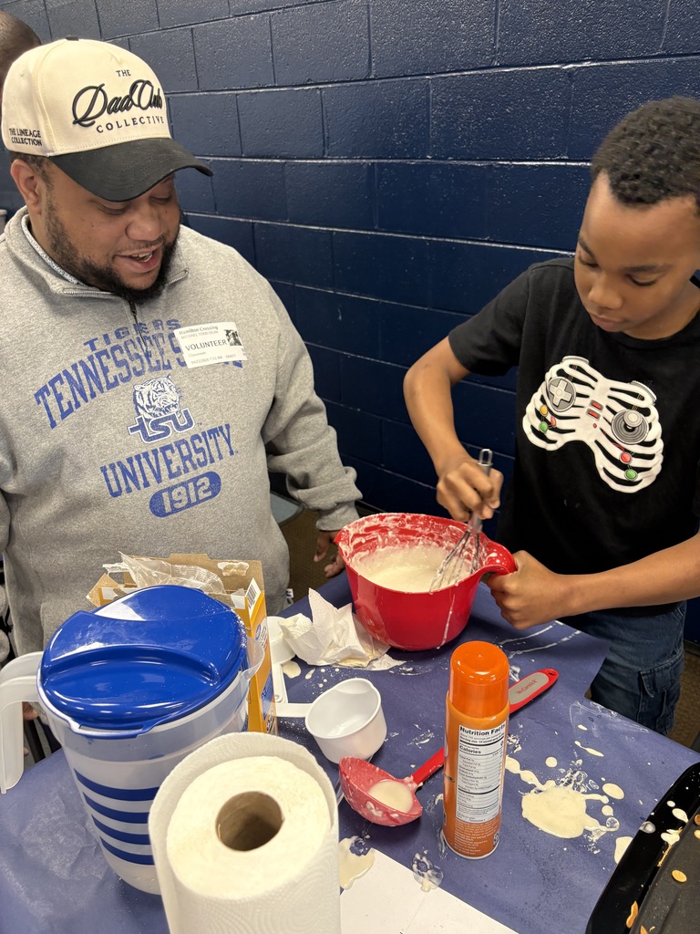 A man and a boy at a table, mixing ingredients in a bowl with spoons.
