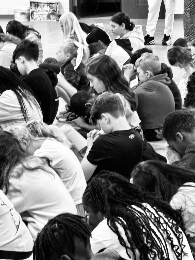 A black-and-white image shows a group of people sitting in a circle, engaged in a discussion.