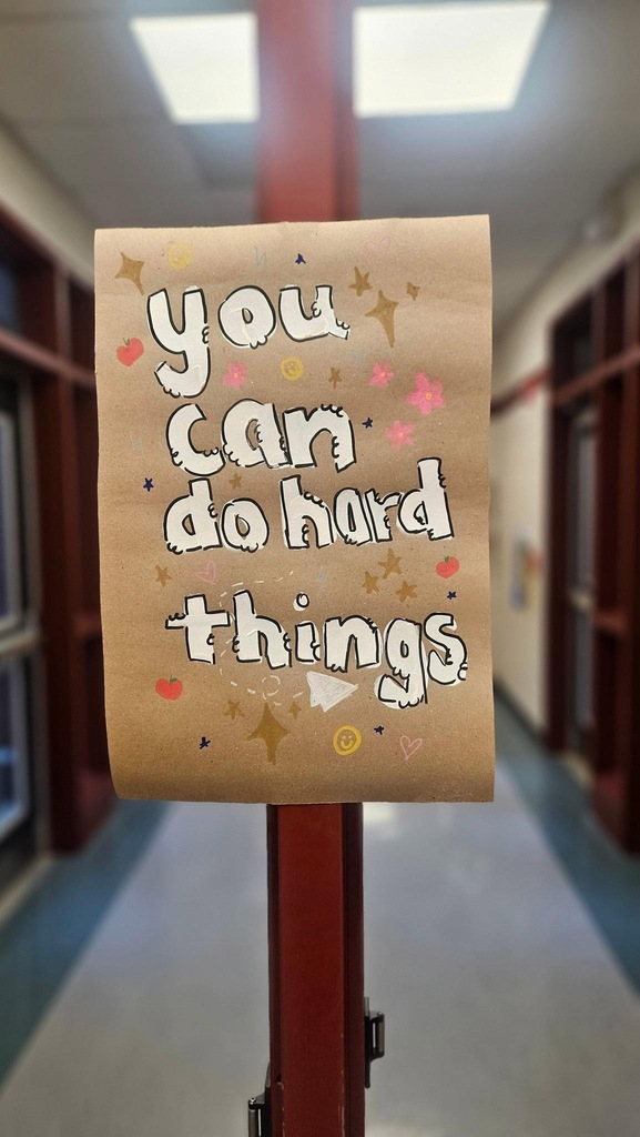 A brown paper sign with white writing and colorful decorations on a red pole. It says, "You can do hard things."