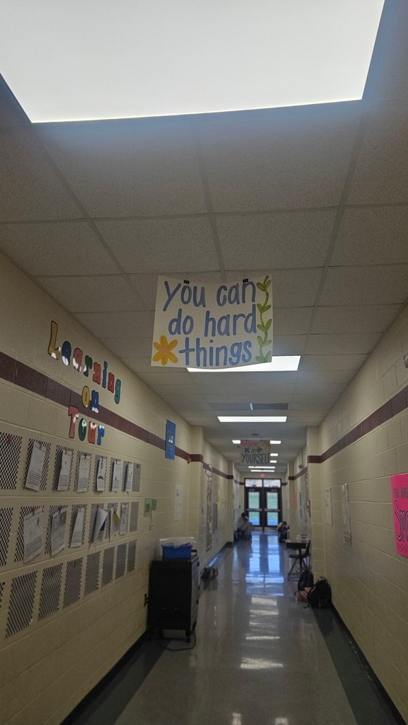 A hallway with white walls and brown trim. A sign reads "You can do hard things". Papers are attached to the walls.