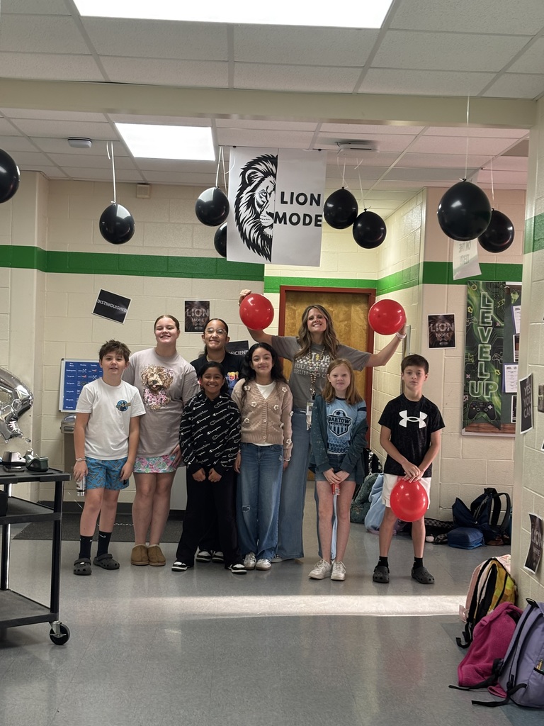 Eight students posing in a room with a banner. A person holds a red balloon.