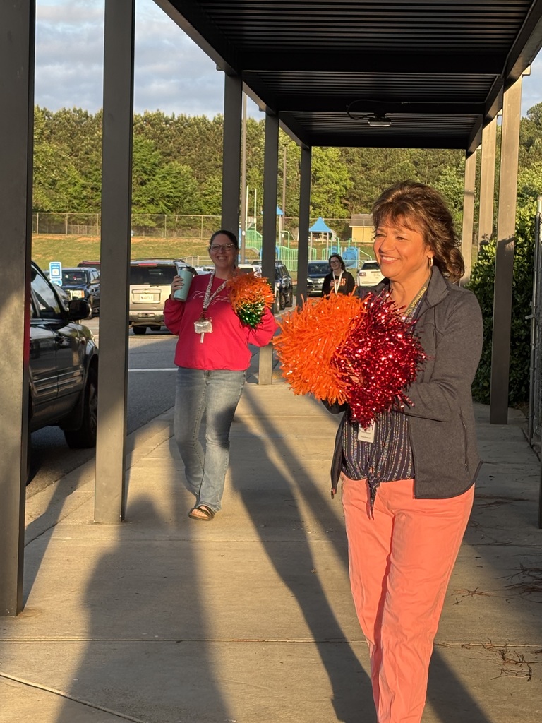 Two women in red and orange pom-poms walk on a covered walkway in a parking lot.