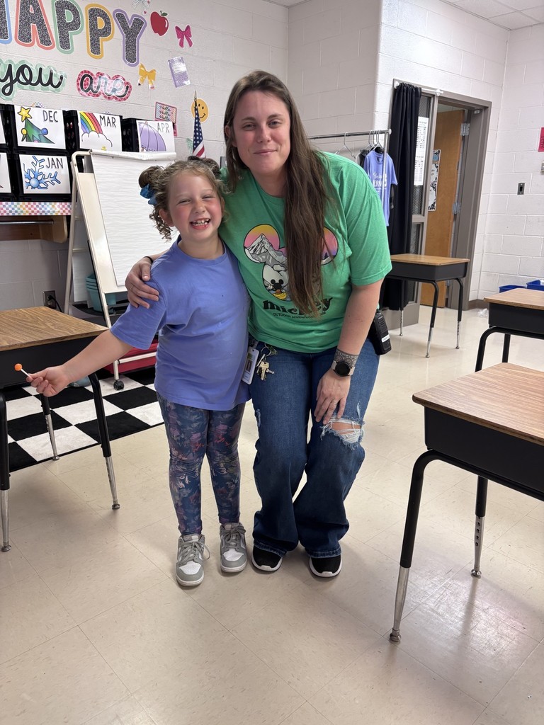 Woman and child in a classroom, smiling, with desks and a white board in the background.