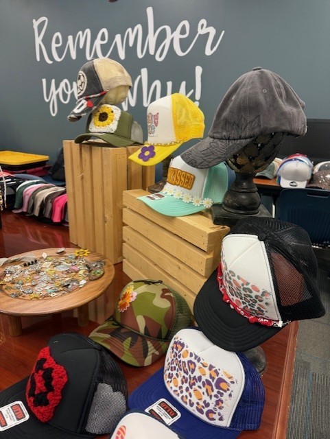 Display of hats, including floral, camouflage, and checkered designs, on a table with wooden storage boxes.