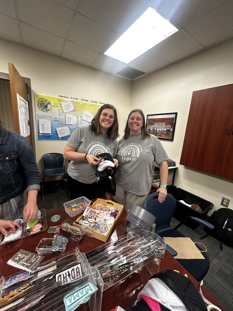 Two women stand in a room with a table full of items, including plastic bags and a box.